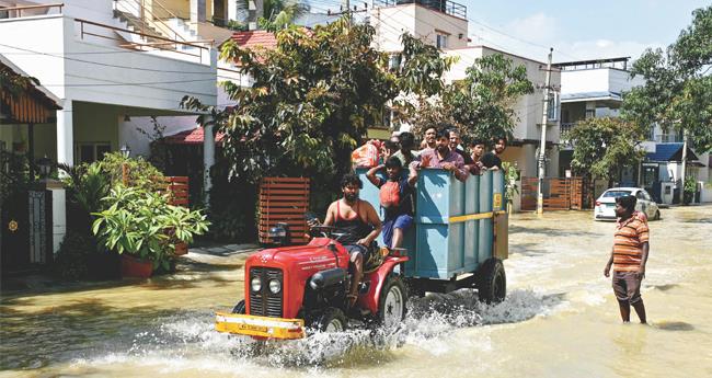 ക​ന​ത്ത മ​ഴ​യെ​ത്തു​ട​ർ​ന്ന് വെ​ള്ളം ക​യ​റി​യ ബം​ഗ​ളൂ​രു​വി​ലെ റോ​ഡി​ലൂ​ടെ 
വാ​ഹ​ന​ത്തി​ൽ സു​ര​ക്ഷി​ത സ്ഥാ​ന​ങ്ങ​ളി​ലേ​ക്കു​നീ​ങ്ങു​ന്ന​വ​ർ